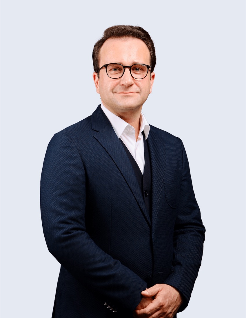 Norman Scherer in dunklem Anzug, Weste und weißem Hemd mit Brille lächelt.